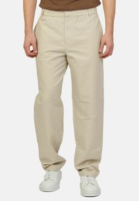 Pantaloni beige leggeri con vita elastica, design dritto e tasche laterali, abbinati a sneakers bianche.