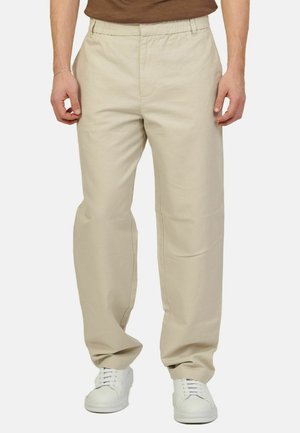 Pantaloni beige leggeri con vita elastica, design dritto e tasche laterali, abbinati a sneakers bianche.