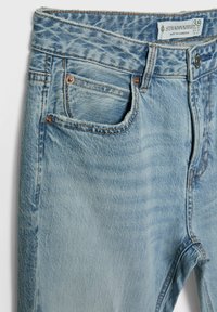 Jean en denim bleu clair montrant le haut devant avec poches, passants de ceinture, rivets en cuivre, bouton et étiquette de taille indiquant 38 de Stradivarius.