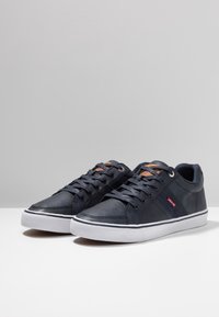 Baskets bleu marine en cuir et textile, dotées de semelles en caoutchouc blanches, d'accents marron et d'une fermeture à lacets.