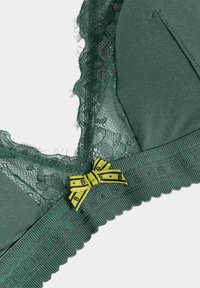 Green bra featuring a lace trim, smooth cups, and a yellow patterned bow detail. Textured straps with decorative edges add visual interest.