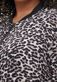 Bomberka w panterkę w kolorach czarnym i beżowym, zapinana na zamek, z prążkowanymi mankietami. Tkanina ma teksturowane wykończenie.