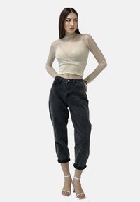Helle beige, semi-transparente, langärmlige Bluse mit Wickeldesign, kombiniert mit lässigen, dunkelgrauen Jeans und weißen Riemchenschuhen.