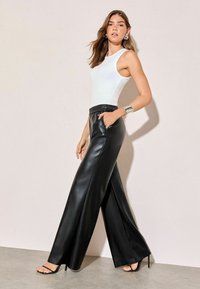 Melna mākslīgās ādas platajām biksēm ar elastīgu jostasvietu, apvienotām ar baltu bez piedurknēm topu. Persona valkā melnas augstpapēžu sandales.