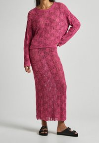 Rosa stickad tvådelad outfit som består av en lös sittande långärmad topp och en matchande lång kjol med en texturerad spetsmönster.