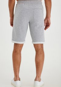 Shorts en coton gris avec une taille élastique, des poignets retroussés et une poche arrière. Portés avec des baskets blanches.