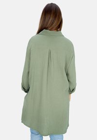 Olivgrünhemd mit Kragen aus strukturiertem Stoff, mit Rückenschlitz und hochrollbaren Ärmeln, in lockerer Passform und längerem Rücken.