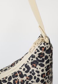 Sac à imprimé léopard avec une fermeture éclair beige, fabriqué en tissu lisse. Il possède une fine sangle réglable et un détail de fermeture éclair bien visible.