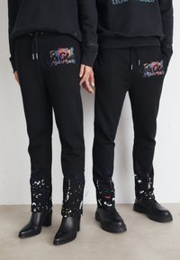 Svart joggebukser med fargerike sprutmønstre, som har frontlommer, justerbar snor innover i livet, og et tapered design på bena.
