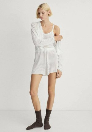 Witte gebreide lounge set met een tanktop en shorts, aangevuld met een lichtgewicht cardigan. Bruine geribde sokken maken de look compleet.