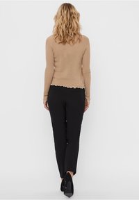 Maglione beige a coste con orlo scallop, abbinato a pantaloni neri e scarpe con tacchi alti. Vista da dietro con capelli lunghi e ondulati in mostra.