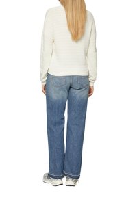 Pull en maille blanche, coupe ample, associé à un jean taille haute bleu clair, avec poches arrière et ourlet effiloché, rehaussé par des baskets.