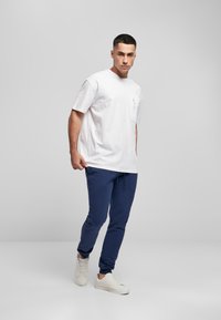 Hvid bomulds T-shirt med lomme, kombineret med mørkeblå joggebukser og hvide sneakers. Outfit'et har en afslappet pasform og et minimalistisk design.