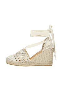 Witte espadrille-wedge met kantdetails, geweven jute zool en stoffen enkelbandjes. Heeft een gesloten teen en textuurelementen.