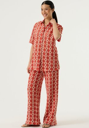 Completo a due pezzi con motivo rosso, composto da camicia a maniche corte con bottoni e pantaloni a gamba larga, con un design geometrico in colori a contrasto.