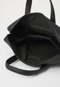 Black textured leather handbag with a zippered opening, featuring fabric lining and multiple interior pockets for organization.