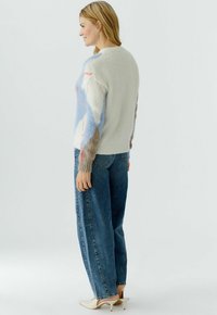 Gebreide trui met textuur in blauw, grijs en crème patronen, gecombineerd met loszittende blauwe jeans en witte pumps met een spits toelopende neus.