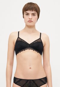 Bralette en dentelle noire avec des panneaux en maille transparente, design en V, bretelles ajustables et bords festonnés, assorti à un bas transparent.