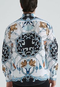 Chemise à boutons avec un motif floral et corde en bleu, noir et beige. Fabriquée en tissu doux, avec des manches longues et un col classique.
