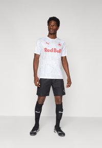 Grå camo-mønstrede trøje med rødt "Red Bull" logo, sorte shorts og sorte sokker med hvidt Puma-logo; athletic fit og sportsdesign.