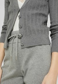 Grå ribbad cardigan med knappar, tillsammans med matchande grå sweatpants med dragband och textilier med struktur.