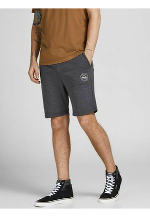 Szare bawełniane szorty sportowe z bocznymi kieszeniami, z białym okrągłym logo na lewej udzie. Noszone z czarnymi sneakersami za kostkę.
