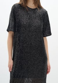 Svart paljettklänning med korta ärmar, med en löst sittande passform, rund halsringning och en texturerad yta skapad av vertikala paljetter.