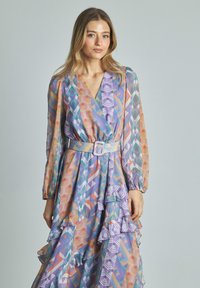 Bunt gemustertes Kleid mit V-Ausschnitt, langen Ärmeln und Rüschenschichten. Besitzt einen taillierten Gürtel. Der Stoff hat eine seidige Textur mit geometrischen Designs.