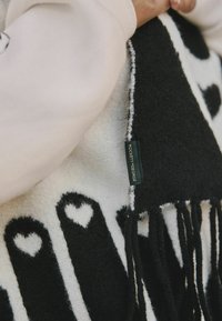 Couverture en noir et blanc avec un motif de cœurs, texture douce, bords frangés, et une étiquette portant la mention "Rockett St George."