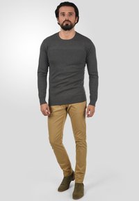 Chemise grise à manches longues, pantalon khaki slim-fit, bottines olivines. Texture lisse, design ajusté, style minimaliste, couleurs neutres.
