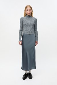 Pilka, siūta iš megztinio audinio, užsegama su užtrauktuku, derinama su sklandžia, šviesiai pilkos spalvos maxi sijonu. Juodi loaferiai ir balti trumpi kojinai užbaigia įvaizdį.