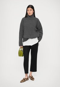 Szary gruby sweter z golfem z dzianiny noszony na białej koszuli, czarne spodnie o szerokich nogawkach, klapki w panterkę i mała zielona torebka.