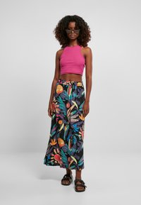 Roze cropped tanktop gecombineerd met een lange zwarte rok met kleurrijke bloemenpatronen. Het model draagt zwarte sandalen, heeft krullend haar en een zonnebril op.