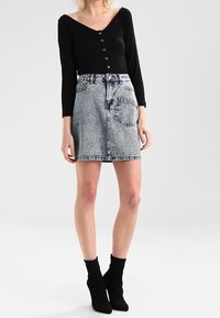 Top negro de manga larga con detalle de botones, combinado con una falda de mezclilla azul clara con bolsillos y un dobladillo sin acabar. Lleva puestos unos botines negros.