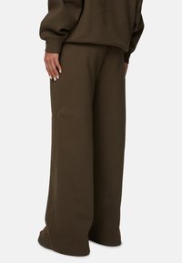 Pantalons de survêtement à jambes larges en vert olive foncé, fabriqués en mélange de coton doux. Présentent une coupe décontractée et un détail de couture minimal au niveau de l'ourlet.