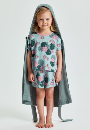 Young girl stands barefoot wearing matching light blue floral and fish print top and shorts with a hooded robe draped over her shoulders.