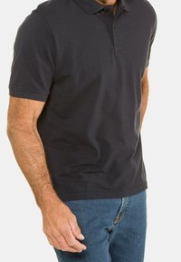 Chemise polo en coton de couleur bleu marine foncé avec un col classique, des manches courtes et un ourlet droit. Portée avec un jean en denim bleu.