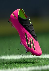 Kirkkaan pinkki jalkapallokenkä, jossa on teksturoidulla päällisellä, mustilla yksityiskohdilla ja vihreillä korostuksilla, virtaviivaisella muotoilulla ja piikkipohjalla.