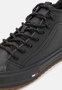 Svarta lädersneakers med svarta snören, rund tå, texturerad gummisula och en sidodekor med röda, vita och blå ränder.