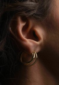 Goldene Creolen mit drei konzentrischen Ringen hängen im Ohr einer Person und zeigen eine glatte, polierte Oberfläche sowie eine glänzende Textur.