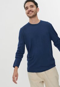 Marineblaue Langarmshirt mit Rundhalsausschnitt aus weichem Stoff. Verfügt über eine lockere Passform und leicht umgeschlagene Bündchen. Kombiniert mit hellbeigen Hosen.