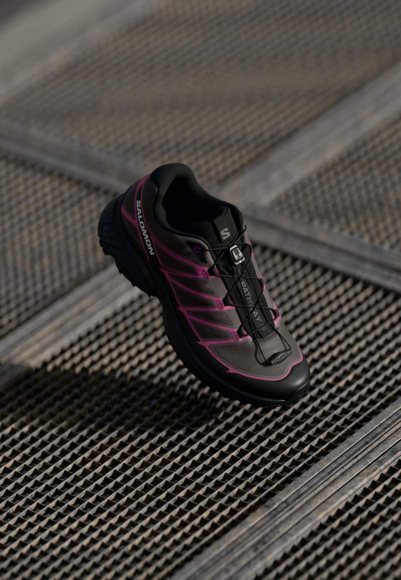 Black and pink running shoe with a textured upper, rounded toe, and integrated lacing system. Features logo and lightweight design.