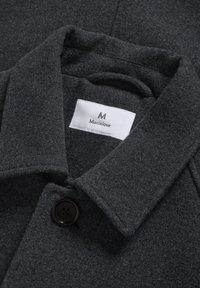 Mörkgrå ullrock med krage, en stor svart knapp och en vit etikett som läser Matinique inuti.