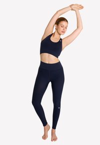 Granatowy sportowy stanik i legginsy z wysokim stanem, wykonane z elastycznego materiału, charakteryzujące się gładką fakturą i minimalną ilością detali z logo.