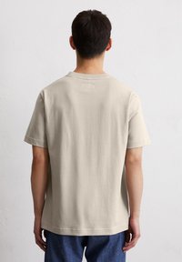 Beige T-Shirt mit kurzen Ärmeln, lässiger Passform, Rundhalskragen und einer kleinen Nahtdetail auf der Rückseite. Weiches Baumwollmaterial.