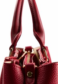 Sac à main en cuir rouge texturé avec doubles poignées, détails en métal doré et fermeture éclair. Présente une forme structurée et des accents lisses.