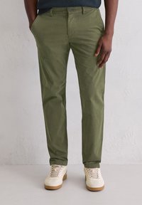 Zielone bawełniane spodnie chino z bocznymi kieszeniami, o wąskim kroju, z płaskim przodem, szlufkami na pasek i gładką fakturą, w połączeniu z beżowymi tenisówkami.