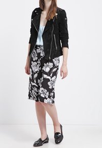 Black suede biker jacket with silver hardware, worn over a light blue top, paired with a black floral knee-length skirt and black loafers.