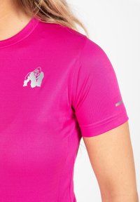 Fuchsia sportshirt met korte mouwen van gladde, rekbare stof. Heeft een zilveren gorilla-logo op de linkerkant van de borst en een reflecterende accent.