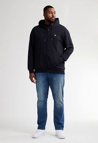 Námořnická mikina s kapucí na zip, s předními kapsami a stahovacími šňůrkami. Doplněná světle modrými džínami a bílými teniskami.